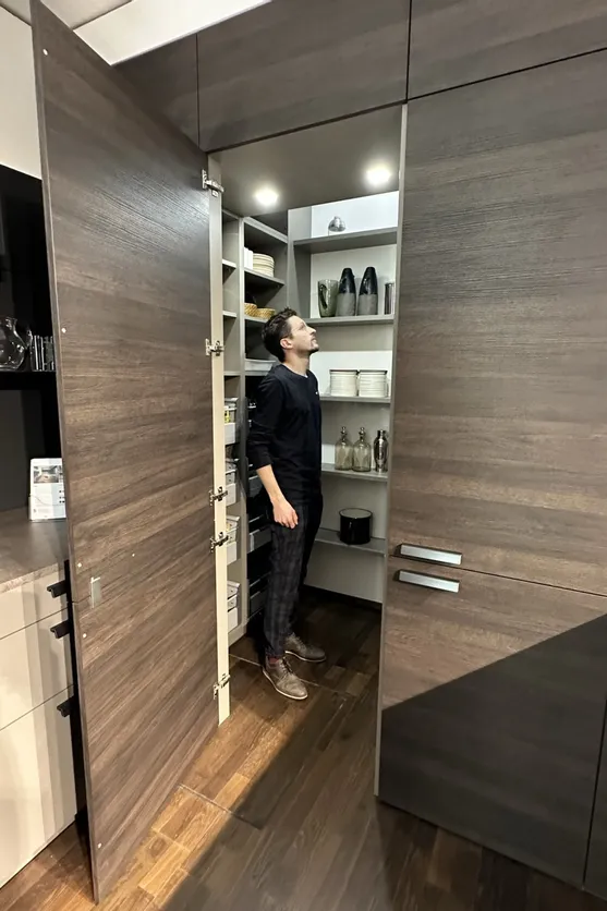 Mann steht in einer modernen Speisekammer mit offenen Regalen und dunklen Holztüren