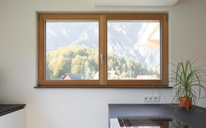 Blick aus Küchenfenster mit Holzrahmen auf herbstlichen Wald und Berge im Hintergrund