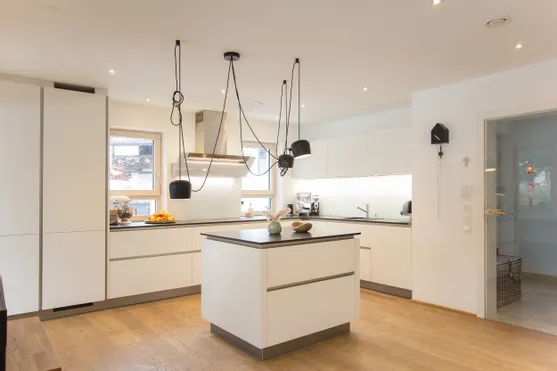 Moderne weiße Einbauküche mit Kücheninsel, Holzfußboden und Hängelampen