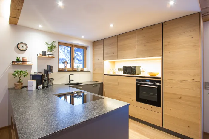 Moderne Küche mit Holzelementen, Kochinsel, eingebautem Backofen und Blick auf verschneite Berge