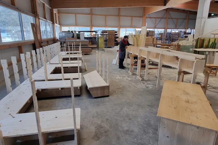 Tischler arbeitet in heller Werkstatt an Holzregalen und Möbelteilen aus hellem Holz