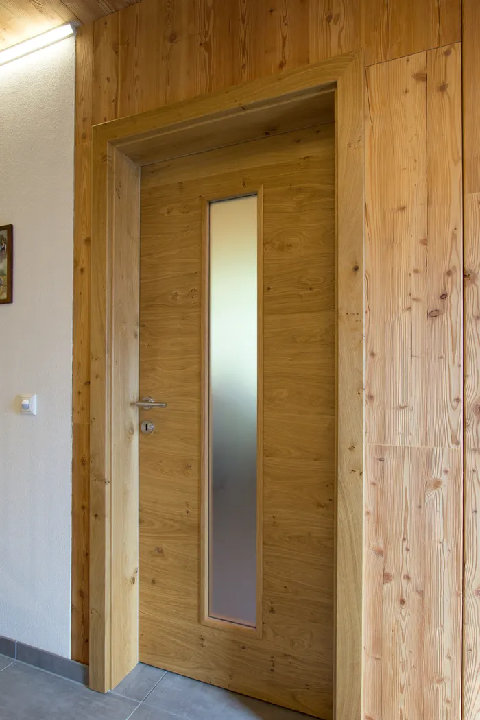 Holztür mit schmalem Milchglasfenster in einem modern verkleideten Innenflur