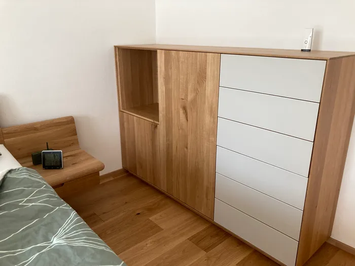 Moderne Holzkommode mit weißen Schubladen neben Bett in minimalistischem Schlafzimmer