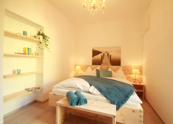 Helles Schlafzimmer mit Holzbett, blauer Decke, Nachttischen und Regalwand