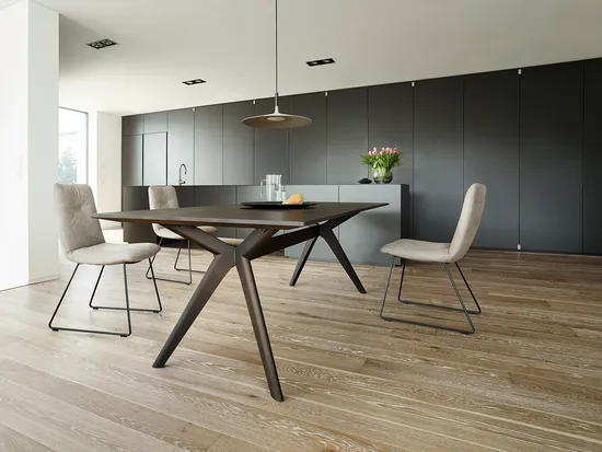 Moderne Küche mit dunklen Schränken, Holztisch, beigen Stühlen und abstrakter Wandkunst