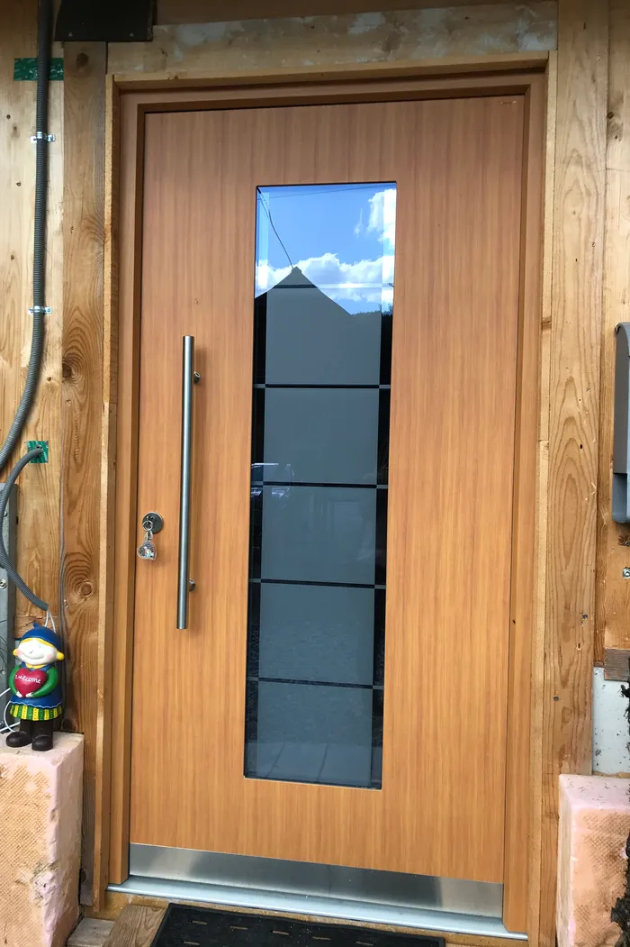 Moderne Holzeingangstür mit Glaseinsatz und Gartenzwerg mit Willkommen-Schild