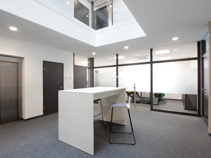 Modernes Büro mit Glastrennwänden, Aufzug, Hochtisch und Barhocker in hellem Ambiente