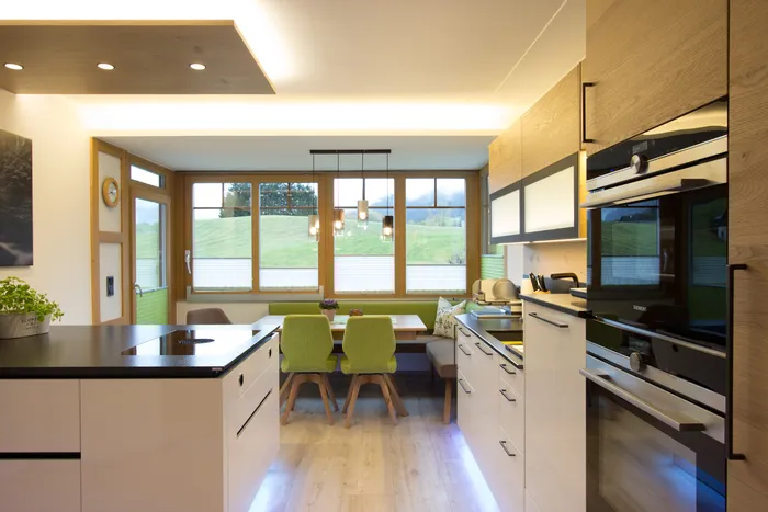 Moderne Wohnküche mit Einbaugeräten, Kochinsel und Essbereich mit grünen Stühlen vor großen Fenstern