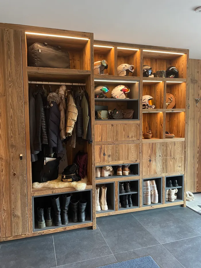 Holzgarderobe mit Winterjacken, Skischuhen, Helmen und Stiefeln ordentlich einsortiert