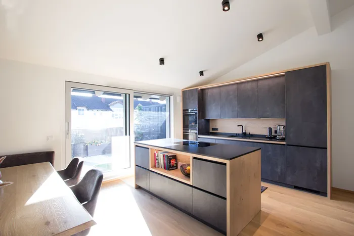 Moderne offene Küche mit Kücheninsel, dunklen Fronten und integriertem Essbereich bei Tageslicht