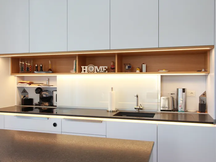 Moderne Einbauküche mit weißen Schränken, schwarzer Arbeitsplatte und LED-Beleuchtung