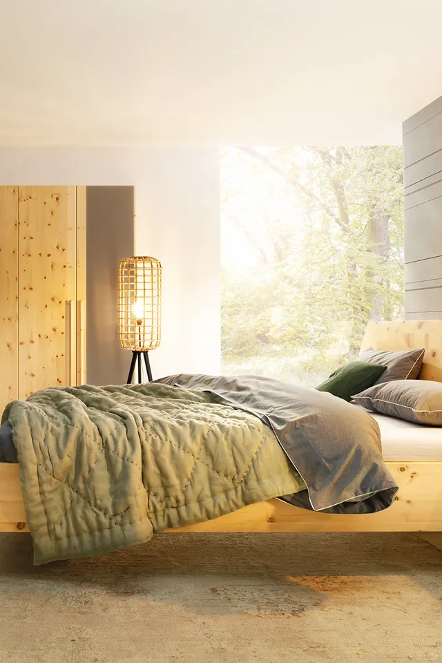 Modernes Schlafzimmer mit Massivholzbett, grünem Bettzeug und großem Holzkleiderschrank bei Tageslicht