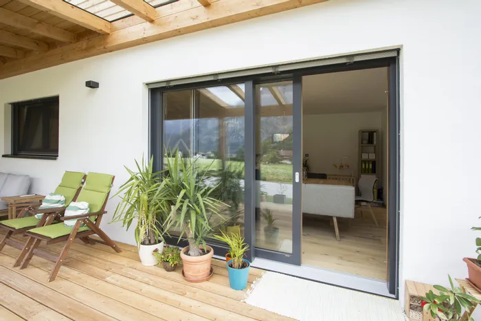 Moderne Terrasse mit Holzboden, grünen Liegestühlen und Pflanzen vor großer Glasschiebetür