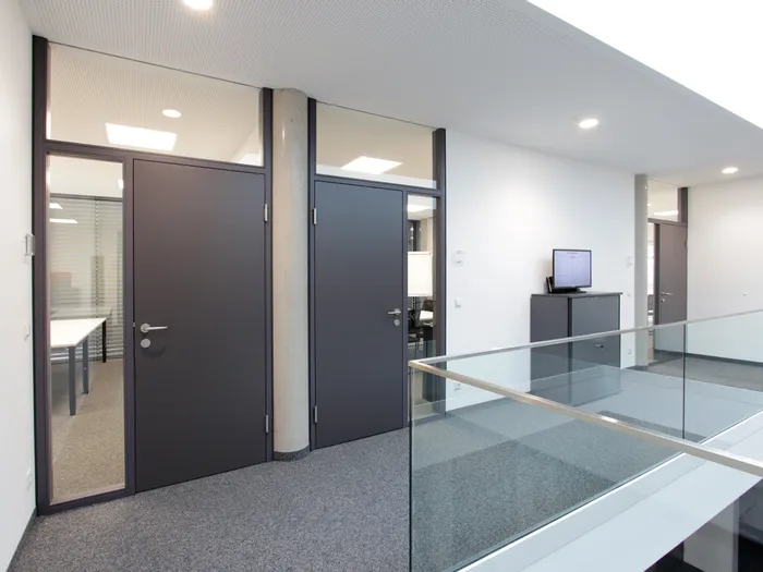 Modernes Bürogebäude mit Glastrennwänden, grauen Türen und Deckenbeleuchtung