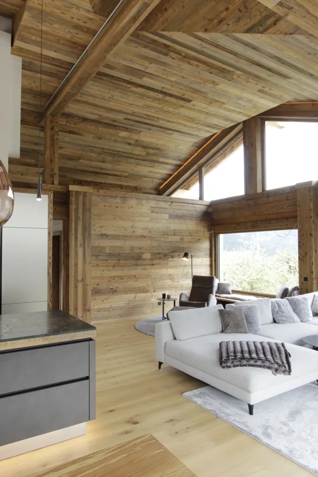 Modernes Chalet-Wohnzimmer mit offener Küche, Holzverkleidung und Panoramafenstern in den Alpen