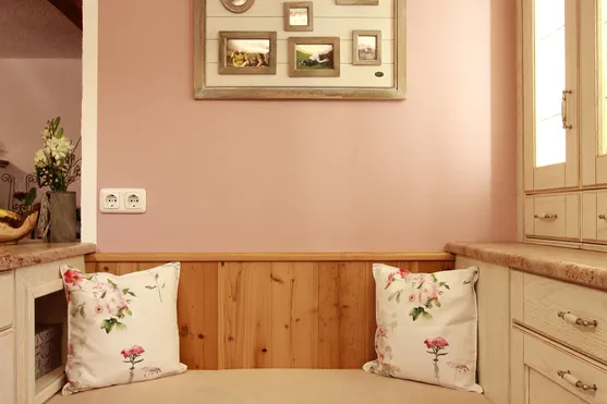 Gemütliche Küchenecke mit Sitzbank, floralen Kissen und Bilderrahmen an rosafarbener Wand