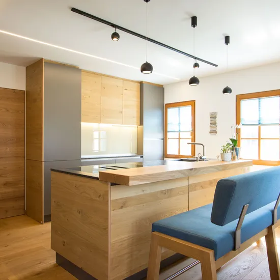 Moderne Küche mit Holzfronten, Kochinsel, Hängelampen und blauer Sitzbank