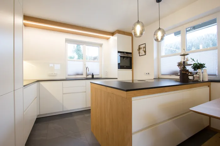 Moderne weiße Küche mit Holzinsel, schwarzen Arbeitsplatten und großen Fenstern