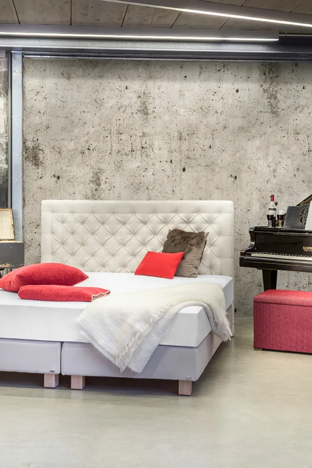 Modernes Boxspringbett in Industrie-Loft mit Klavier und roten Dekokissen