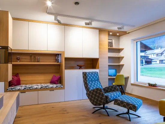 Modernes Wohnzimmer mit Einbauschränken, Lesesessel und großem Fenster mit Blick aufs Dorf