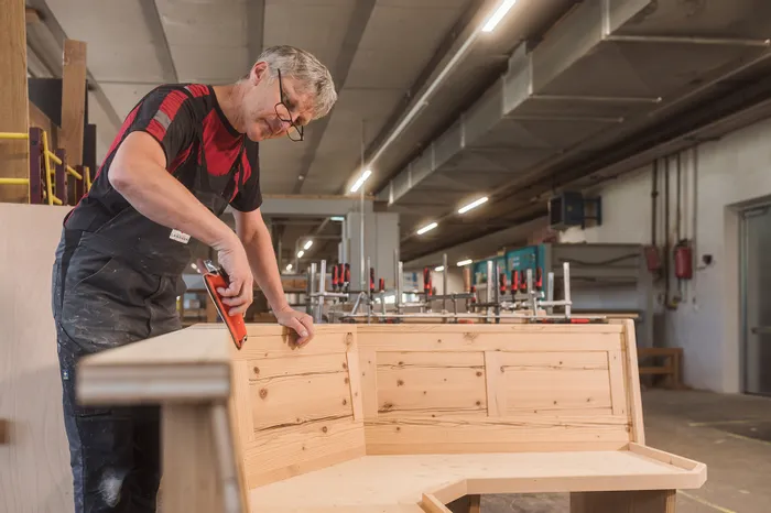 Tischler arbeitet in Werkstatt an einer massiven Eckbank aus Holz mit einem Tacker