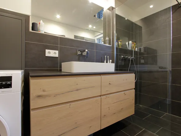 Modernes Badezimmer mit Holzwaschtisch, Glasdusche und Waschmaschine