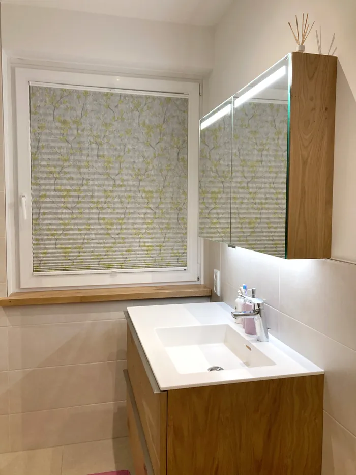 Modernes Badezimmer mit Holzwaschtisch, beleuchtetem Spiegelschrank und gemustertem Plissee am Fenster