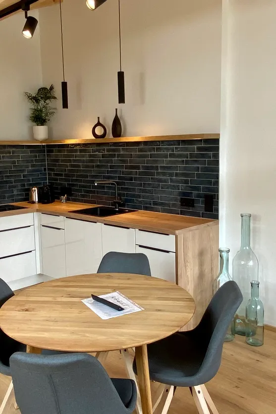 Moderne Einbauküche mit Holzelementen, schwarzer Fliesenrückwand und rundem Esstisch mit vier Stühlen