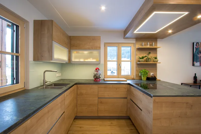 Moderne Einbauküche mit Holzfronten, dunkler Arbeitsplatte und Kräutertöpfen am Fenster