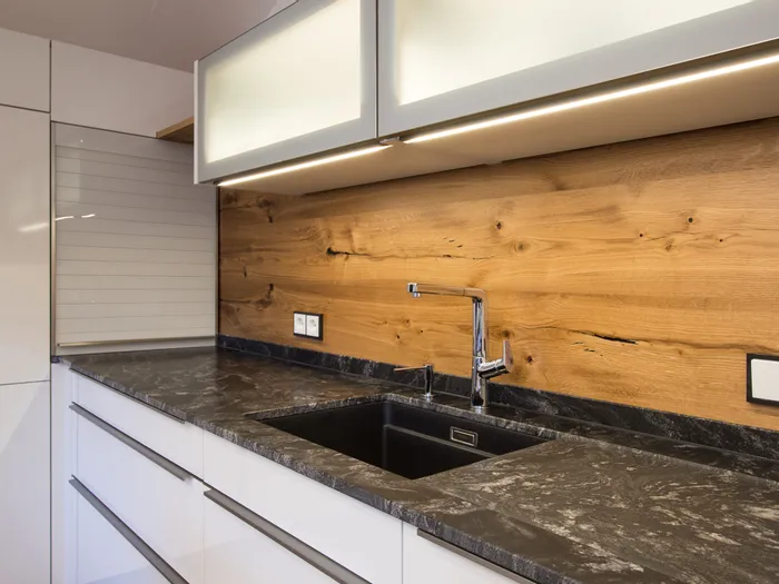 Moderne Küche mit schwarzer Stein-Arbeitsplatte, Holzrückwand und integriertem Spülbecken