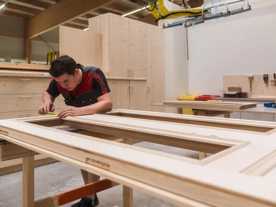 Tischler misst präzise ein Holzrahmenstück in einer modernen Schreinerwerkstatt