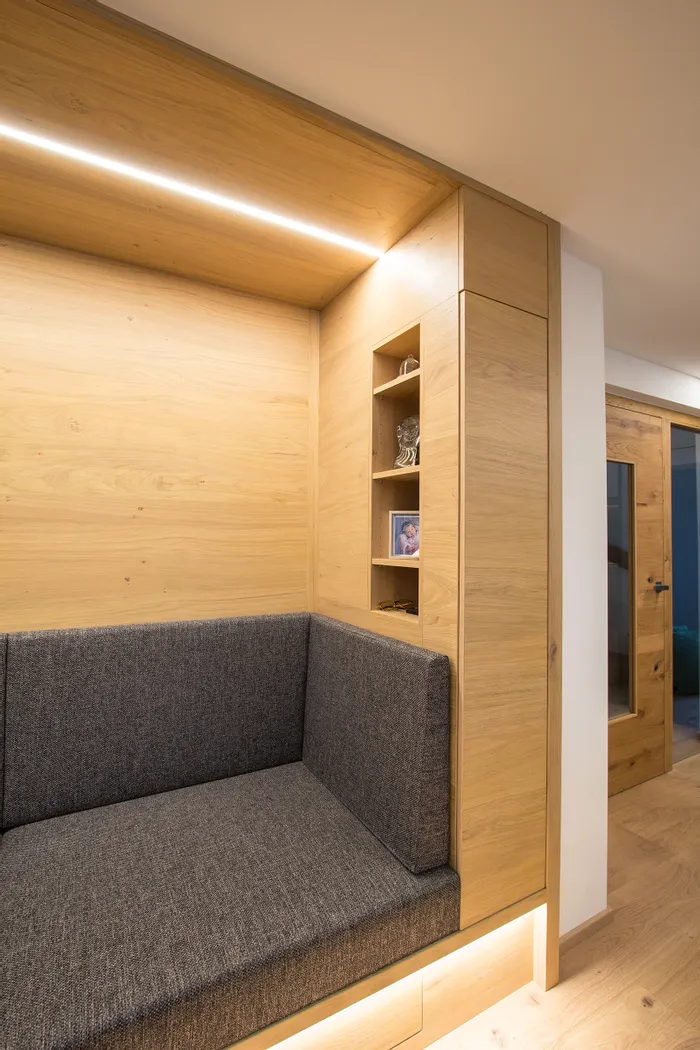 Moderne Sitzbank mit grauem Polster und Holzverkleidung mit integrierten Regalen und LED-Beleuchtung