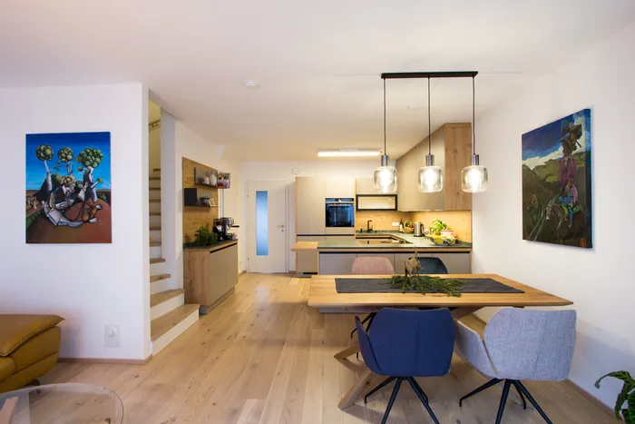 Moderne offene Wohnküche mit Holzboden, Esstisch, Designlampen und stilvoller Wandkunst