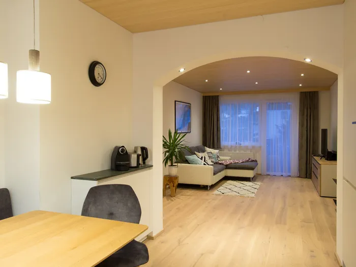 Modernes Wohnzimmer mit Ecksofa, Holzboden, Esstisch und offener Küche bei warmem Licht