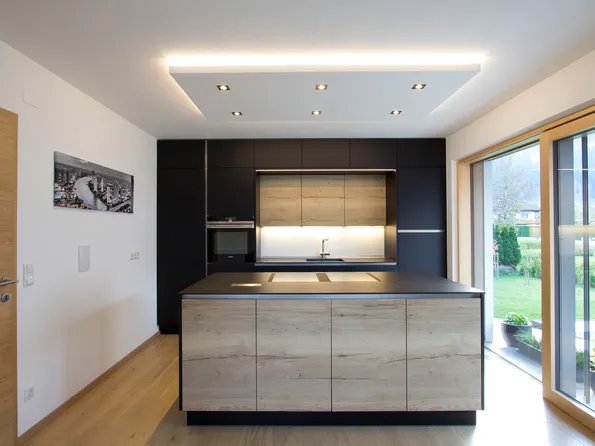 Moderne offene Küche mit Kochinsel in Holz- und Schwarzoptik mit Blick auf Garten