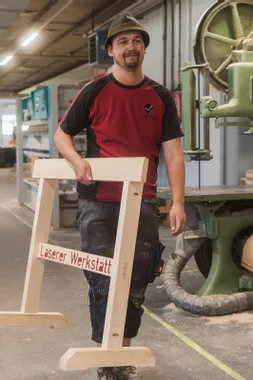 Schreiner trägt Holzgestell mit Aufschrift Laserer Werkstatt in einer Tischlerei