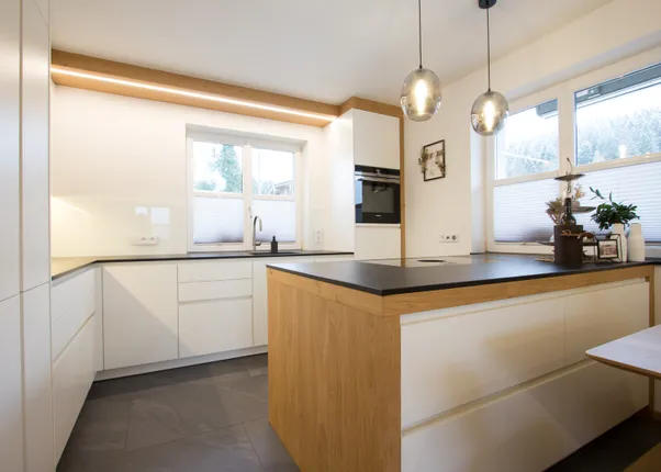 Moderne weiße Küche mit Holzinsel, schwarzen Arbeitsplatten und großen Fenstern