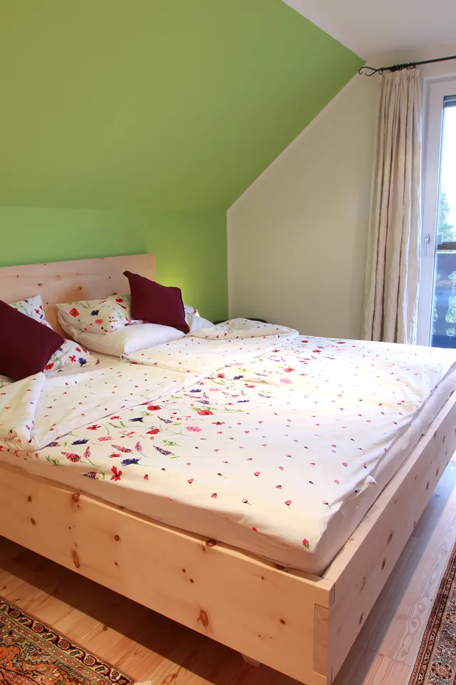 Helles Schlafzimmer mit Doppelbett aus Holz, Bettwäsche mit Blumenmuster und Zugang zum Balkon