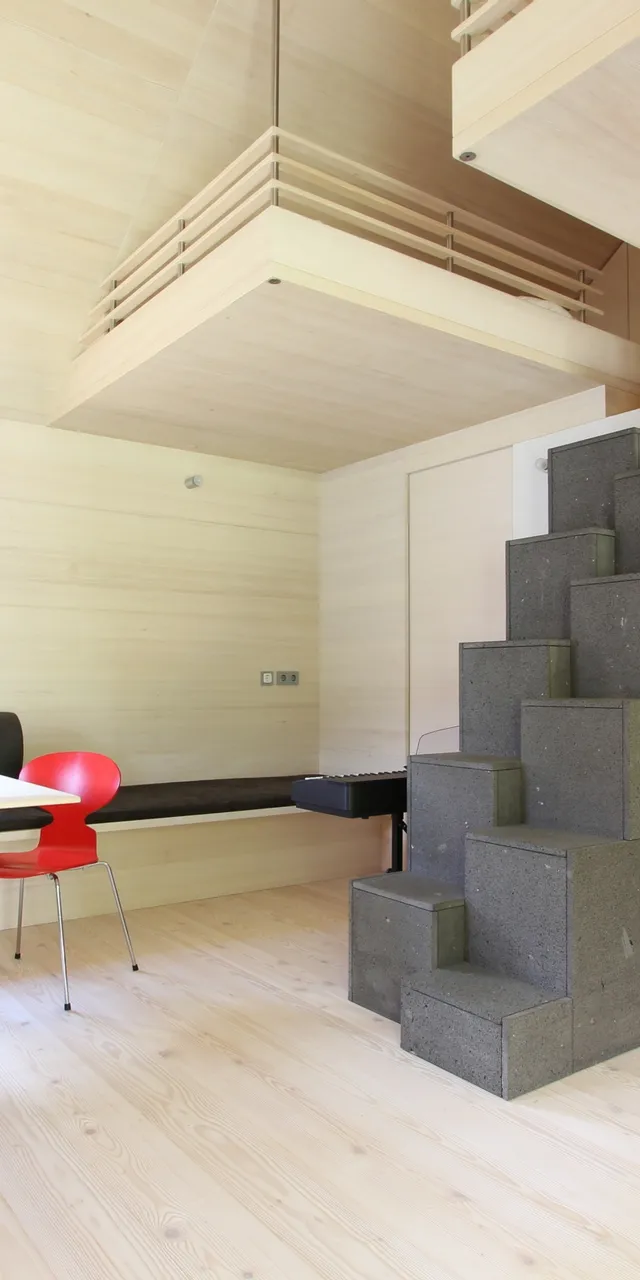 Helles minimalistisches Wohnzimmer mit Holzverkleidung, Esstisch, modernen Stühlen und grauem Treppenofen