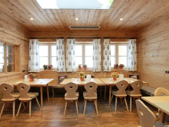 Gemütliches Restaurant mit Holzwänden, dekorierten Tischen und weißen Vorhängen im Alpenstil