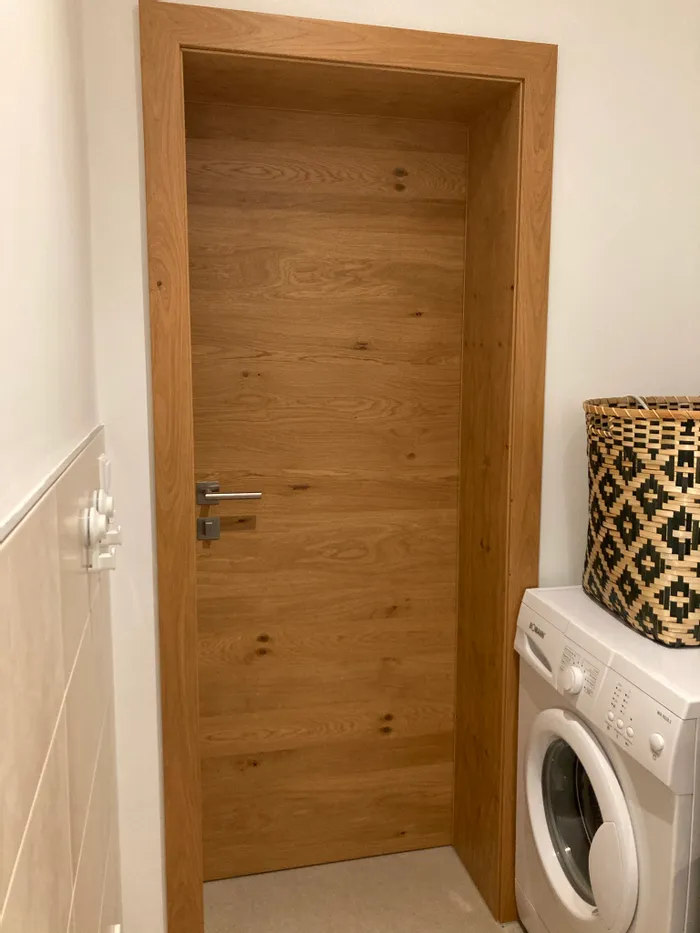 Holztür im Badezimmer neben Waschmaschine mit geflochtenem Wäschekorb