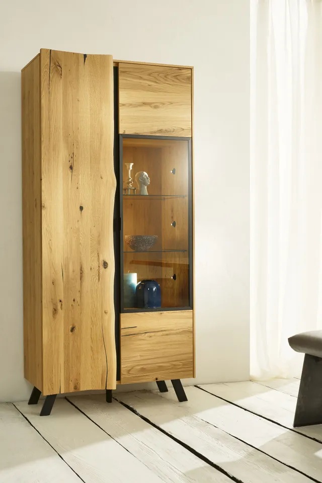 Vitrine aus hellem Massivholz mit Glastür und schwarzen Metallbeinen im modernen Wohnzimmer