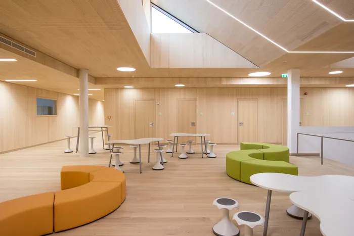 Heller Raum mit modernen Tischen, Hockern und farbigen Sitzbänken in Orange und Grün