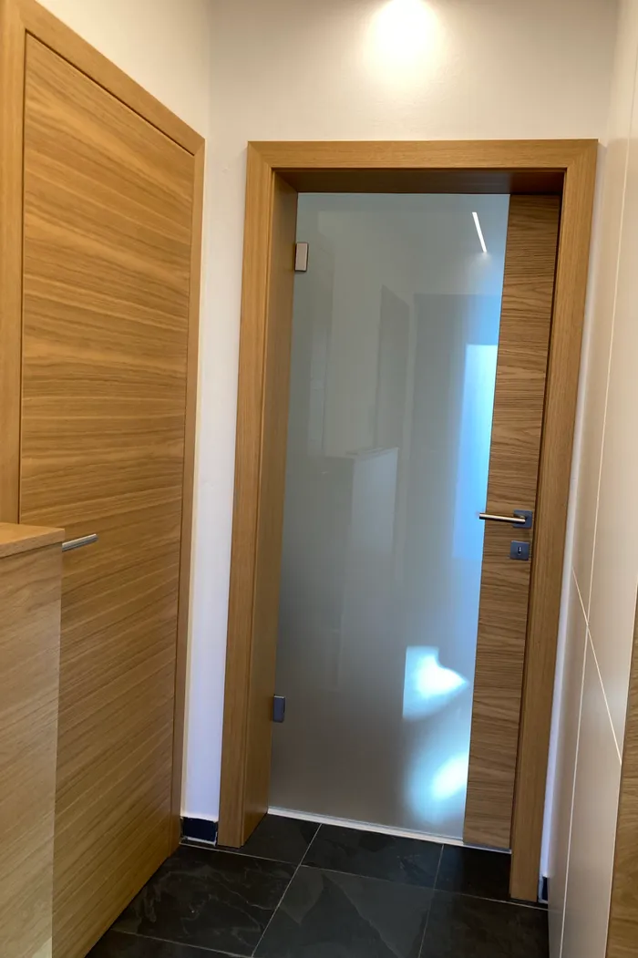 Moderne Innentür aus Milchglas mit Holzrahmen in einem Flur mit dunklen Fliesen