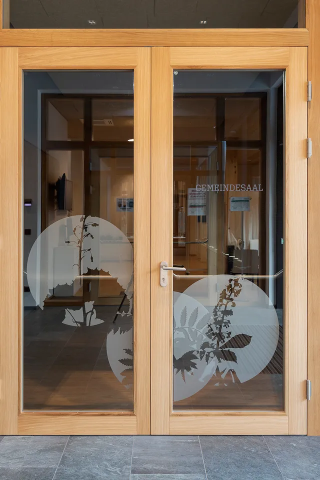 Holztür mit Glaseinsätzen und Pflanzenmotiven, Eingang zum Gemeindesaal