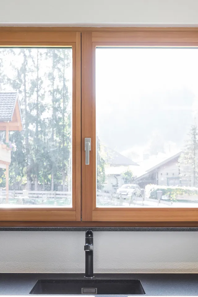 Moderne Küche mit Holzfenster, Blick auf Alpenhaus, Orchidee und Kaffeemaschine auf schwarzer Arbeitsplatte