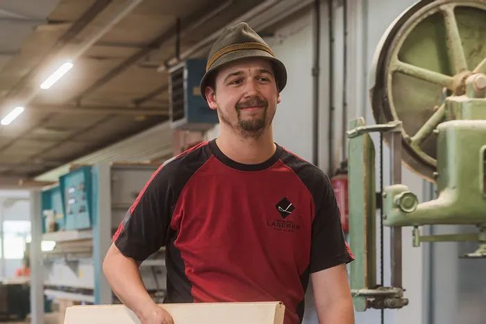 Schreiner trägt Holzgestell mit Aufschrift Laserer Werkstatt in einer Tischlerei