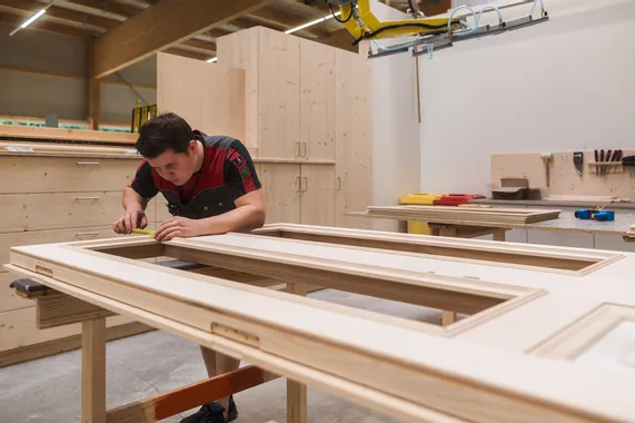 Tischler misst präzise ein Holzrahmenstück in einer modernen Schreinerwerkstatt