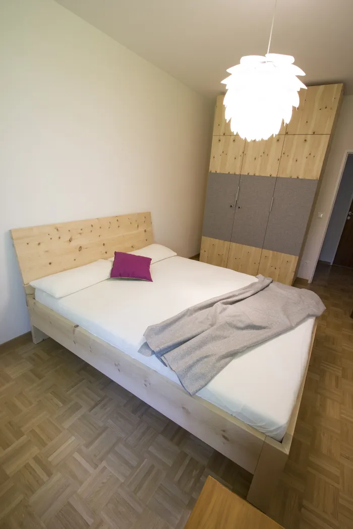 Modernes Schlafzimmer mit Holzbett, violettem Kissen, grauer Decke und Einbauschrank