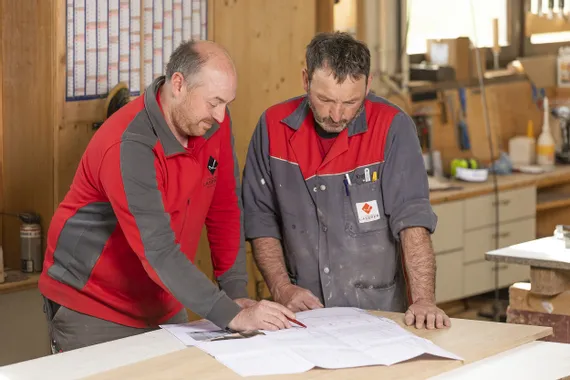 Zwei Handwerker prüfen Bauzeichnungen in einer Holzwerkstatt
